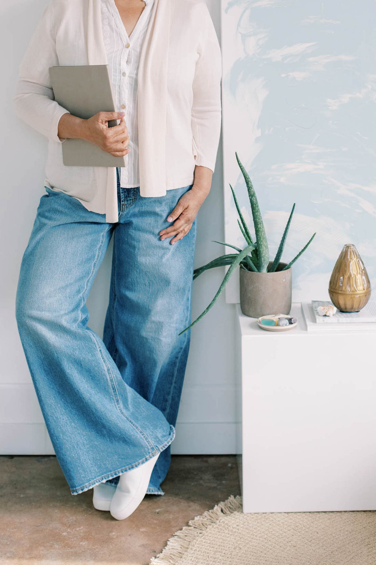 A woman in jeans and a black blazer with black shoes kneeling to count her hundos.