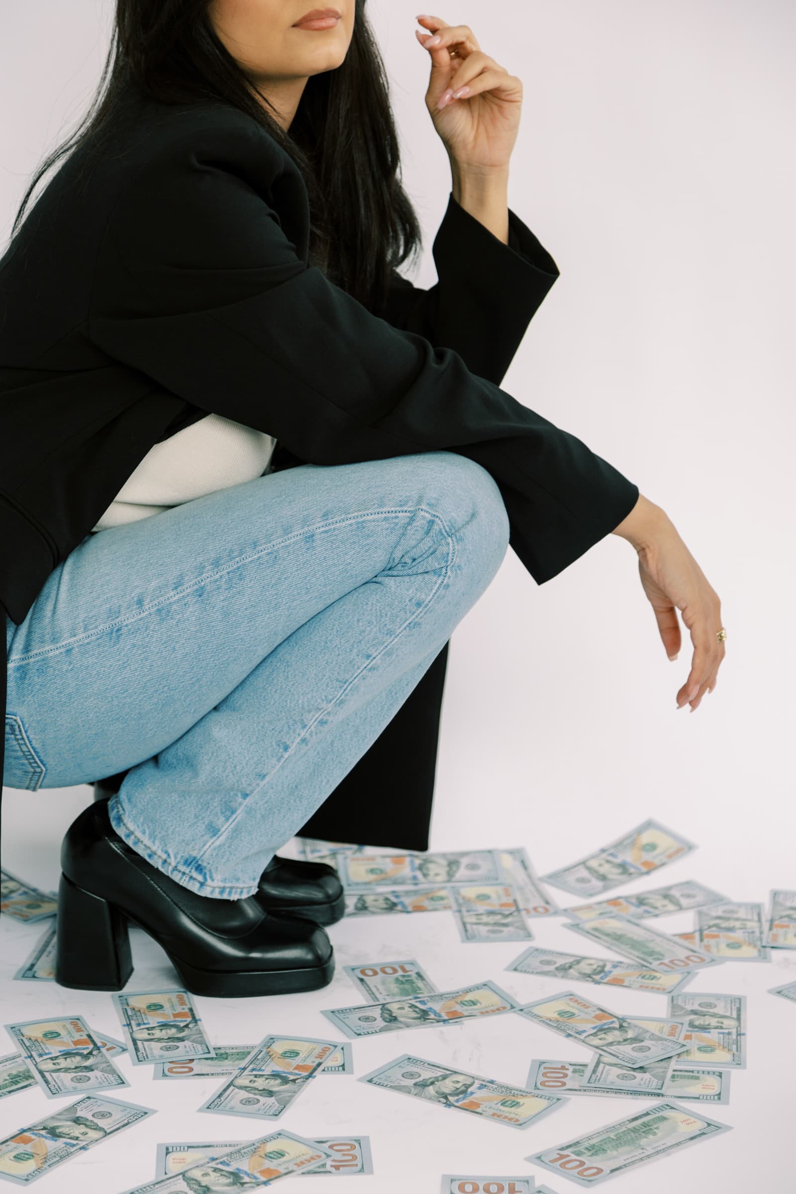 A woman in jeans and a black blazer with black shoes kneeling to count her hundos.